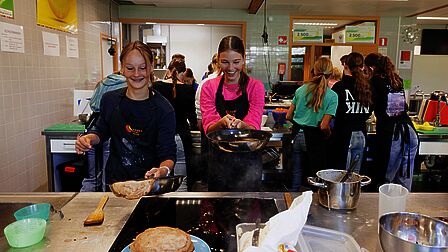 Twee leerlingen bakken pannenkoeken en proberen de pannenkoek in de lucht te gooien. 
